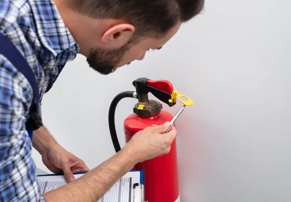 A young male technician is checking the symbol on a fire extinguisher to ensure proper safety and functionality in Long Island, NY.