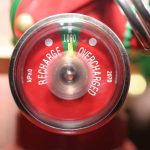 A close-up view of a fire extinguisher pressure gauge showing markings for “Recharge” and “Overcharged,” with the needle pointing to the green zone indicating proper pressure.