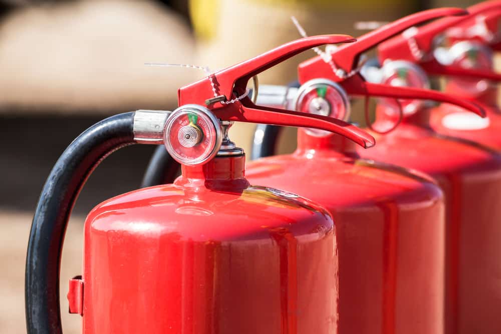 A close-up view of several red fire extinguishers arranged in a row, showing their handles, pressure gauges, and black hoses.